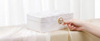 Hand unlocking a white embossed 2-layer lockable jewelry box with round gold clasp and tassel key