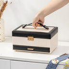 Hand carrying black and white 3-layer jewelry box by leather top handle on white table