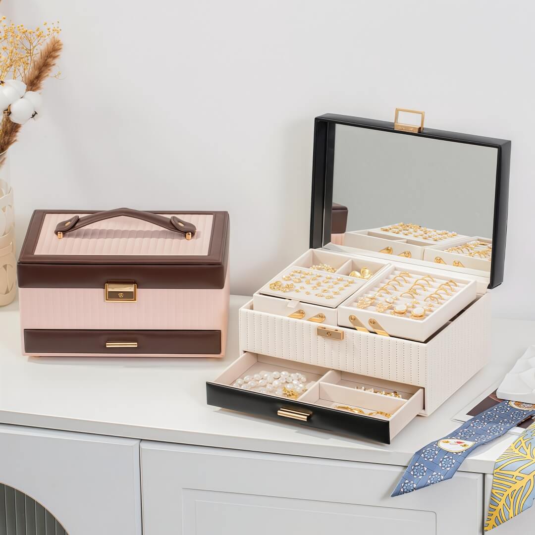 Black and white 3-layer jewelry box open on white dresser with brown and pink closed box beside it, lifestyle scene