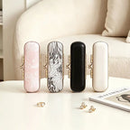 Four mini travel jewelry boxes standing vertically in a row showing variations of pink floral embroidery, grey jacquard fabric, sleek black leather, and smooth white leather with gold kiss-lock clasps.