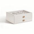 White 2-layer stackable jewelry box with glass lid and gold geometric knobs, being lifted