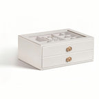 White 2-layer stackable jewelry box with glass lid and gold geometric knobs, being lifted