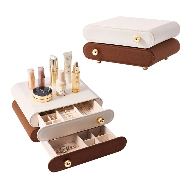 A two-tier stackable leather jewelry organizer with open drawers showing slots for rings, necklaces, and watches, topped with skincare products on a white background.