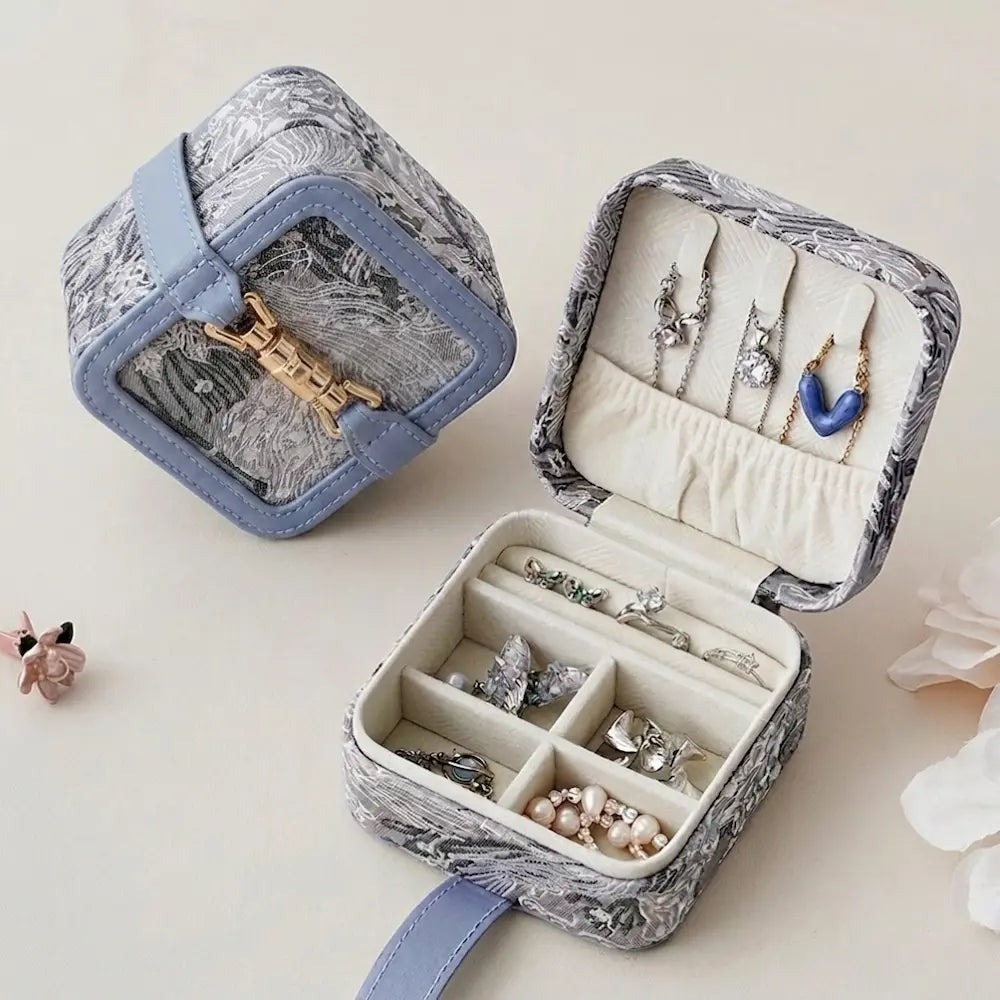Mini lock clasp jewelry box open showing earring slots, necklace hooks, and 4-grid ring compartment in blue floral brocade pattern