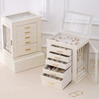 Two cream-white leather jewelry boxes with gold handles; one is open to show a top display compartment, five pull-out drawers, and a side glass door with hanging necklace hooks, displaying full storage capacity.