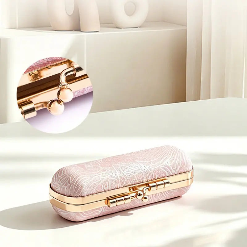 A pink jacquard mini jewelry box featuring a close up circle zoom of its vintage gold kiss-lock clasp mechanism.