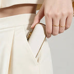 A woman putting a sleek cream white mini jewelry case with a gold clasp into her pant pocket, showcasing its compact pocket-size design.