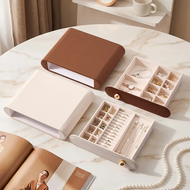 Disassembled view of cream and brown stackable jewelry boxes on a marble table, showcasing removable velvet drawers.