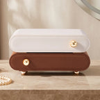 Front view of two closed minimalist jewelry boxes stacked together in cream white and brown leather, featuring sleek gold knob handles and rounded edges.