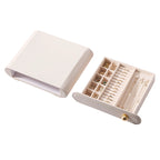 A cream white leather jewelry case with an open drawer filled with organized rings and gold necklaces.